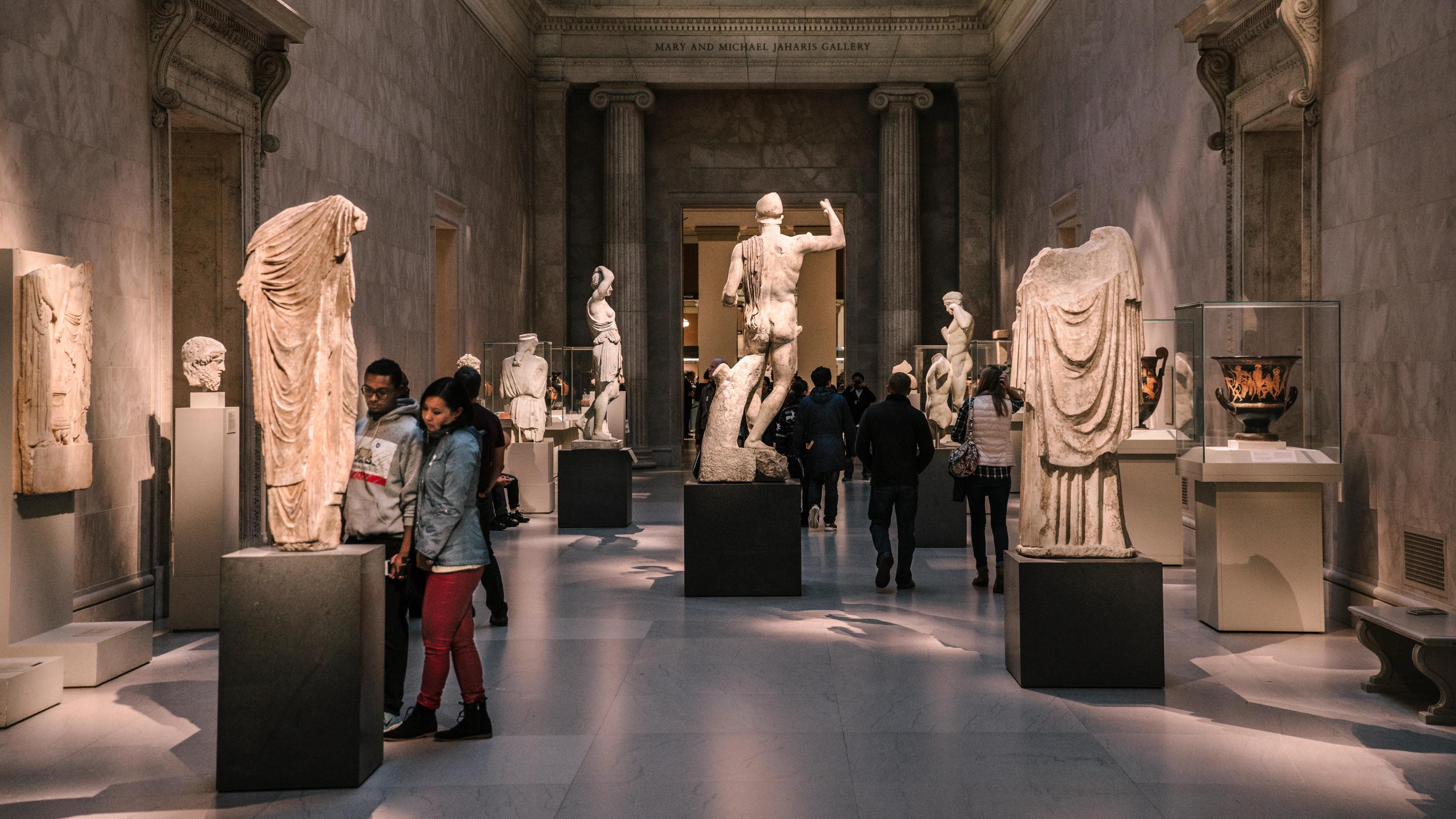 A darkly lit gallery with white marble statues of men and women.