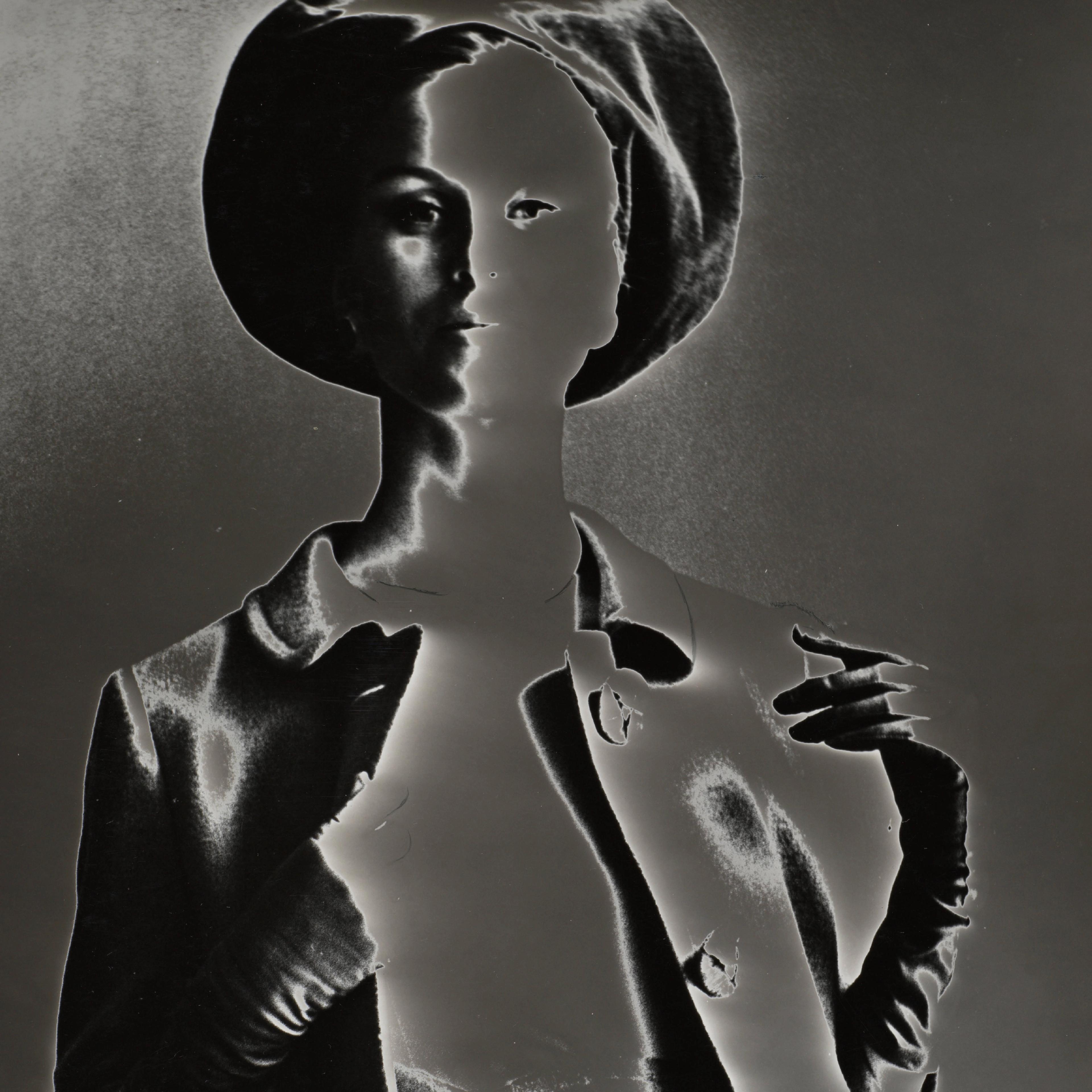 A stylized black-and-white image of a person wearing a hat and jacket, with high contrast and negative effect